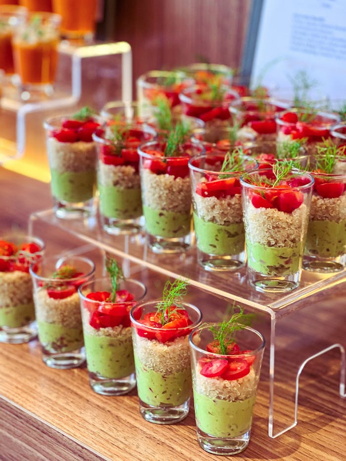 Vibrant avocado, quinoa, and tomato appetizers in shot glasses on display, perfect for events.